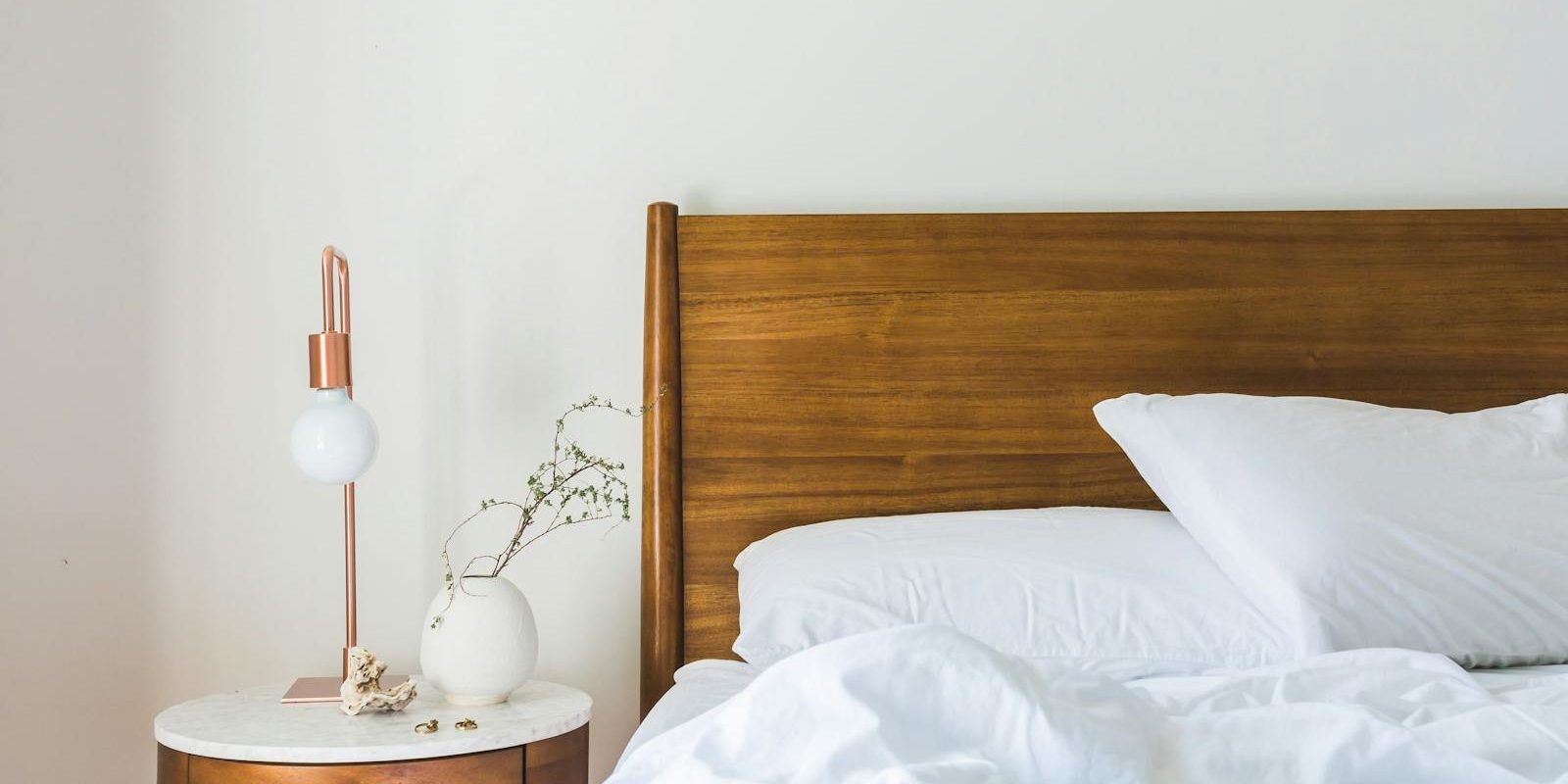 White Bedspread Beside Nightstand With White and Copper Table Lamp