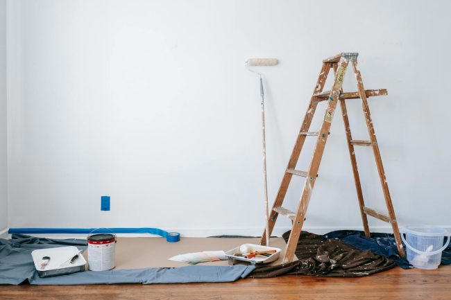 Photo by Blue Bird A room prepared for renovation with a ladder, paint supplies, and drop cloth.